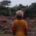 boy wearing brown coat looking on trees in shallow focus photography