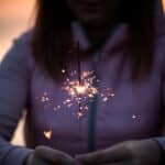 A woman in a hoodie holds a lit sparkler in her hands