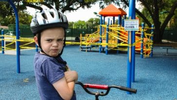 boy in blue denim vest and helmet riding red bicycle