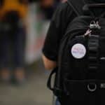 A white“Facts matter” pin on a black backpack on a person's back