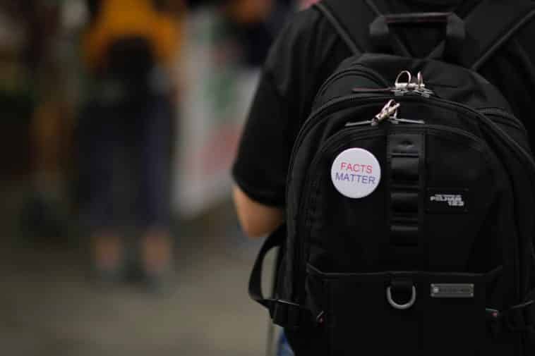 A white“Facts matter” pin on a black backpack on a person's back
