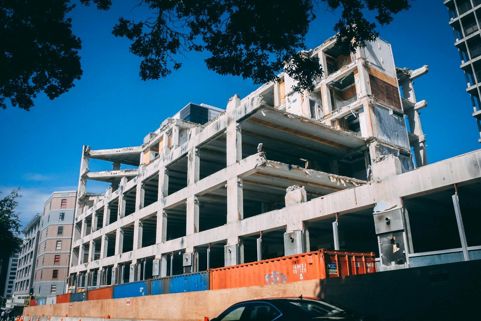 Vraag aan hotelbranche: Wanneer zijn jullie gestopt met het nobele en dienstbare vak van hotelier te bedrijven en onderdeel van de asielindustrie geworden? A partially demolished building under clear blue skies, showcasing urban decay and modern architecture.